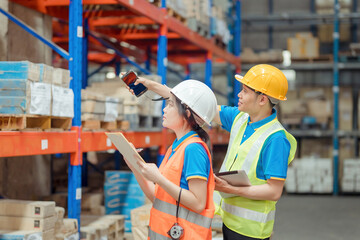 Asian engineer in helmets order and checking goods and supplies on shelves with goods background in...