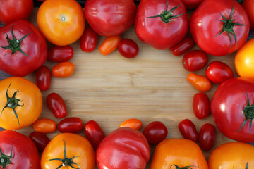 Frame with different sorts of tomatoes on wooden table, flat lay. Space for text