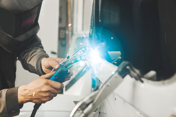 Welder in protective mask welds car body.