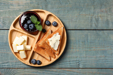 Fototapeta na wymiar Tasty toasts with butter and blueberries on light blue wooden table, top view. Space for text