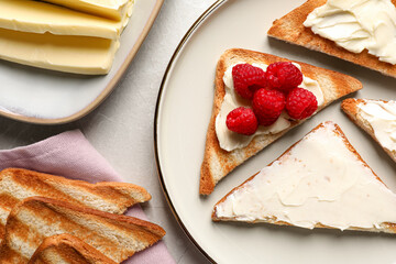 Tasty toasts with butter and raspberries on light grey table, flat lay