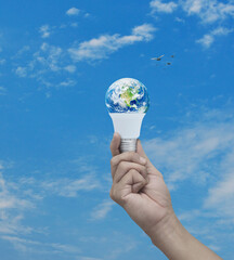Hand holding earth globe inside led light bulb over blue sky, white clouds and birds, Green ecology and saving energy concept, Elements of this image furnished by NASA