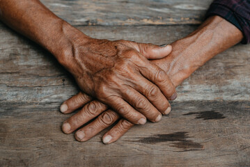 Close-up of old man's hands resting on wood.