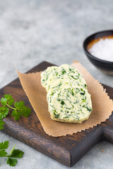 Butter with parsley and salt, cut into circles, on a brown wooden board on a gray concrete background. Types of butter for serving dishes.