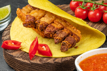 Crispy appetizer of deep-fried pork belly -chicharones wrapped in flatbread and spicy pepper pieces, close-up.