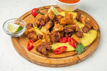 Crispy pieces of pork belly served on a wooden board with a tortilla.