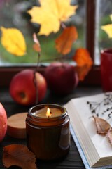 Beautiful burning candle and book on wooden table near window. Autumn atmosphere
