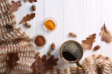 Cup of hot drink, spices, leaves and knitted scarf on white wooden table, flat lay. Cozy autumn atmosphere