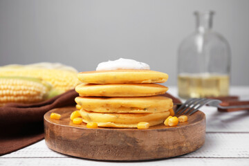 Tasty corn pancakes with sweet kernels and sauce served on white wooden table, closeup