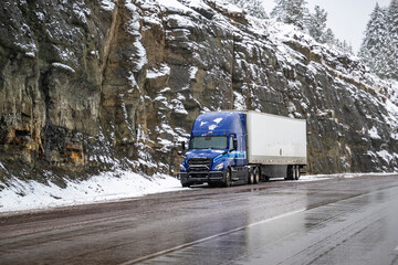 Blue big rig semi truck with dry van semi trailer standing on the top of the mountain pass at winter snowfall time