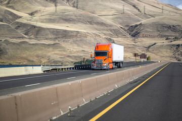 Bright orange long haul big rig semi truck with grille guard transporting cargo in dry van semi...