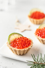 Festive New Year appetizer tartlets stuffed with red caviar and a slice of lime close up on a white tray with text space. Christmas or new year holiday party concept