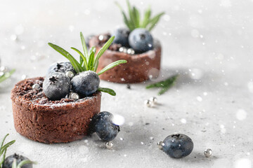 Chocolate brownies decorated with blueberries and rosemary on white textured background with bokeh lights. Christmas, New Year recipe concept. Close up, copy space