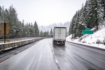 Commercial big rig semi truck with dry van semi trailer transporting cargo running on the wet highway road at winter snow condition