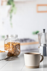 Fototapeta na wymiar Cup of morning coffee on white tile tabletop in kitchen. Healthy breakfast consept with coffee and muesli. Text space