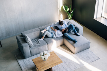Loving couple holding hands, relaxing on cozy sofa in modern living room top view