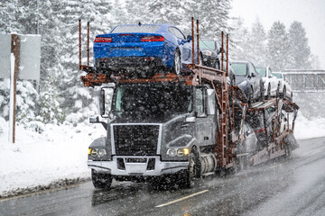 Dark gray car hauler big rig semi truck tractor transporting cars on modular semi trailer driving...