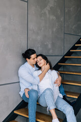 Naklejka premium A young couple in love is sitting on the stairs of their house