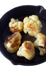 Cauliflower fried, in a cast iron frying pan with olive oil. Isolated on a white background