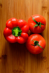 Two fresh red tomatoes and a paprika pepper with drops on a wooden table. Wooden background.