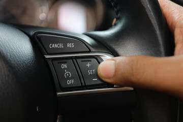 the driver's hand presses the cancel button to set the cruise control feature on modern cars. ...