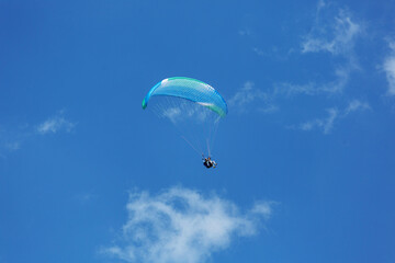 Blue Paraglider flying into the sky with clouds on a sunny day