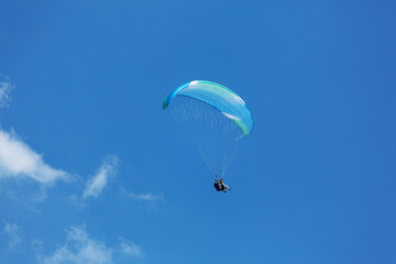 Blue Paraglider flying into the sky with clouds on a sunny day