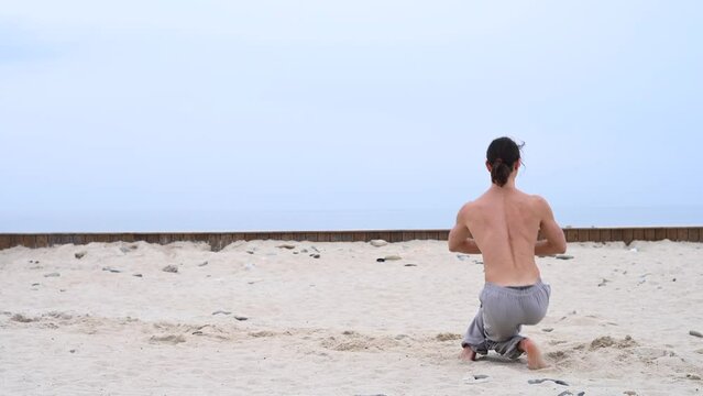 Caucasian man with naked torso practicing wushu on the seashore. 