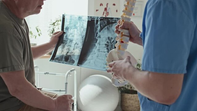 Close-up of doctor showing the problem with spine on skeleton model while patient examining his x-ray image