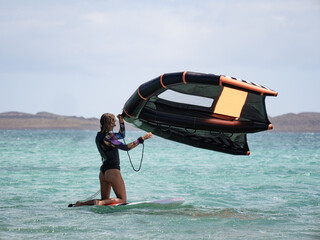 Young woman in the ocean holding wingfoil wing after falling practicing hydrofoil