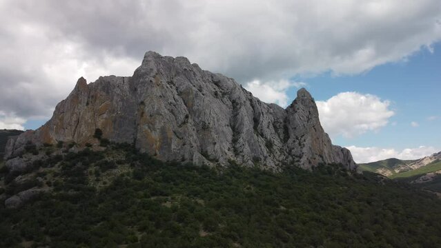 Landscape of a rocky hill surrounded by greenery under a blue cloudy sky