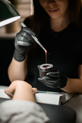 gloved hands of manicurist holding jar and brush with gel polish