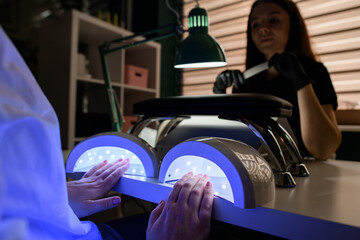 Fototapeta na wymiar Female hand drying nails in ultraviolet lamp in beauty salon.