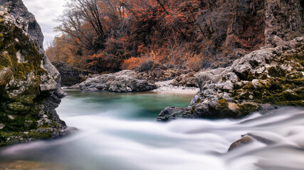Mountain river surrounded by autumn colors. Torrente Torre near the Crosis waterfall, Tarcento, Udine province, Friuli Venezia Giulia region, Italy. Long exposure photography.