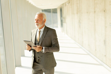 Mature businessman standing with digital tablet in the office corridor