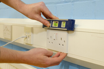 Close-up of electrician using spirit level to check alignment of UK double wall socket in office