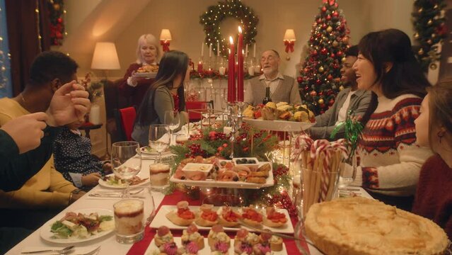 Happy large family sitting at table and celebrating Christmas or New Year at home. Grandmother set the table with traditional dish turkey. Warm atmosphere of family Christmas dinner. Christmas Eve.