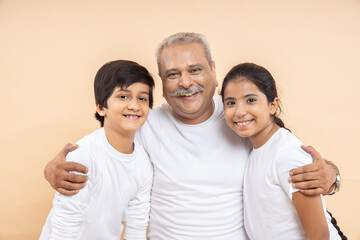 Happy indian senior man with kids wearing white casual t-shirt standing over isolated beige...