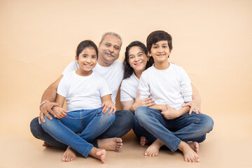 Happy indian grandparents with kids wearing white casual t-shirt sitting together over isolated...