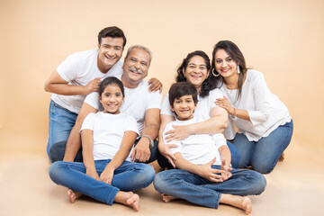  Portrait happy indian asian multi generational family wearing white t-shirt  sitting against beige...