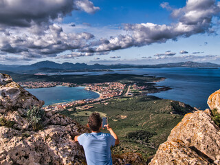 Ragazzo con il cellulare fotografa una meravigliosa vista panoramica di Golfo Aranci, dalla cima della montagna