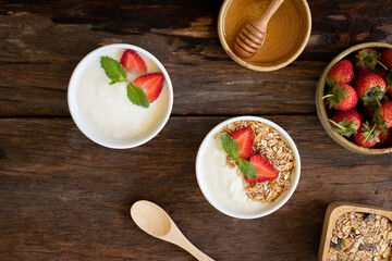 Top view of Strawberry yogurt in a wooden bowl with granola, honey, mint and fresh strawberry on  wooden background. Health food concept.