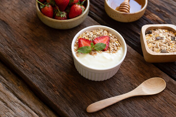 Strawberry yogurt in a wooden bowl with granola, honey, mint and fresh strawberry on  wooden background. Health food concept.
