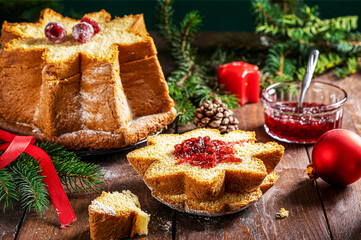 Traditional Italian Christmas cake Pandoro cut in slices on wooden table with Christmas decoration, red fruit jam