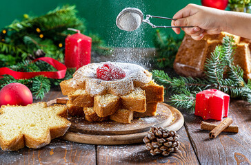 Traditional Italian Christmas cake Pandoro cut in slices on wooden table with Christmas decoration. Child hand is powdering ice sugar on top
