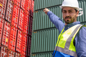 A professional male worker wearing a helmet and uniform points to containers.  A handsome male...