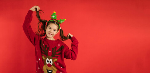 cute little girl with a cute facial expression posing in a Christmas sweater on a bright red background emotional, funny