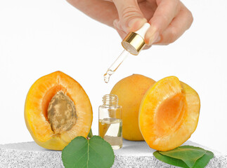 Pipette with essential apricot oil in a female hand. Cosmetic bottle with face serum and fresh apricots