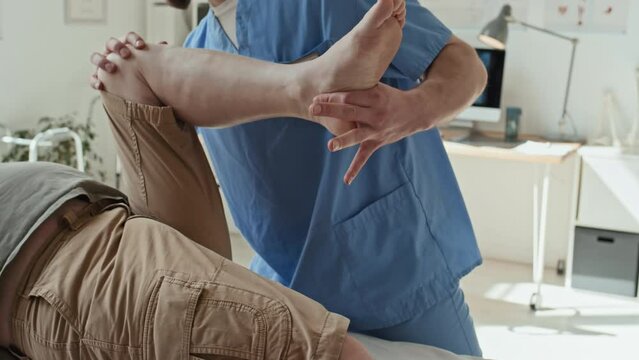 Close-up of physiotherapist stretching leg of patient while he lying on couch at hospital