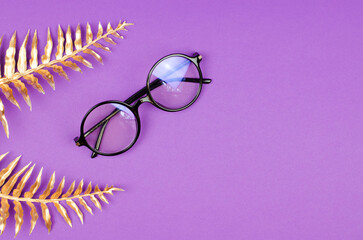 Stylish female glasses on a purple background with golden palm leaves